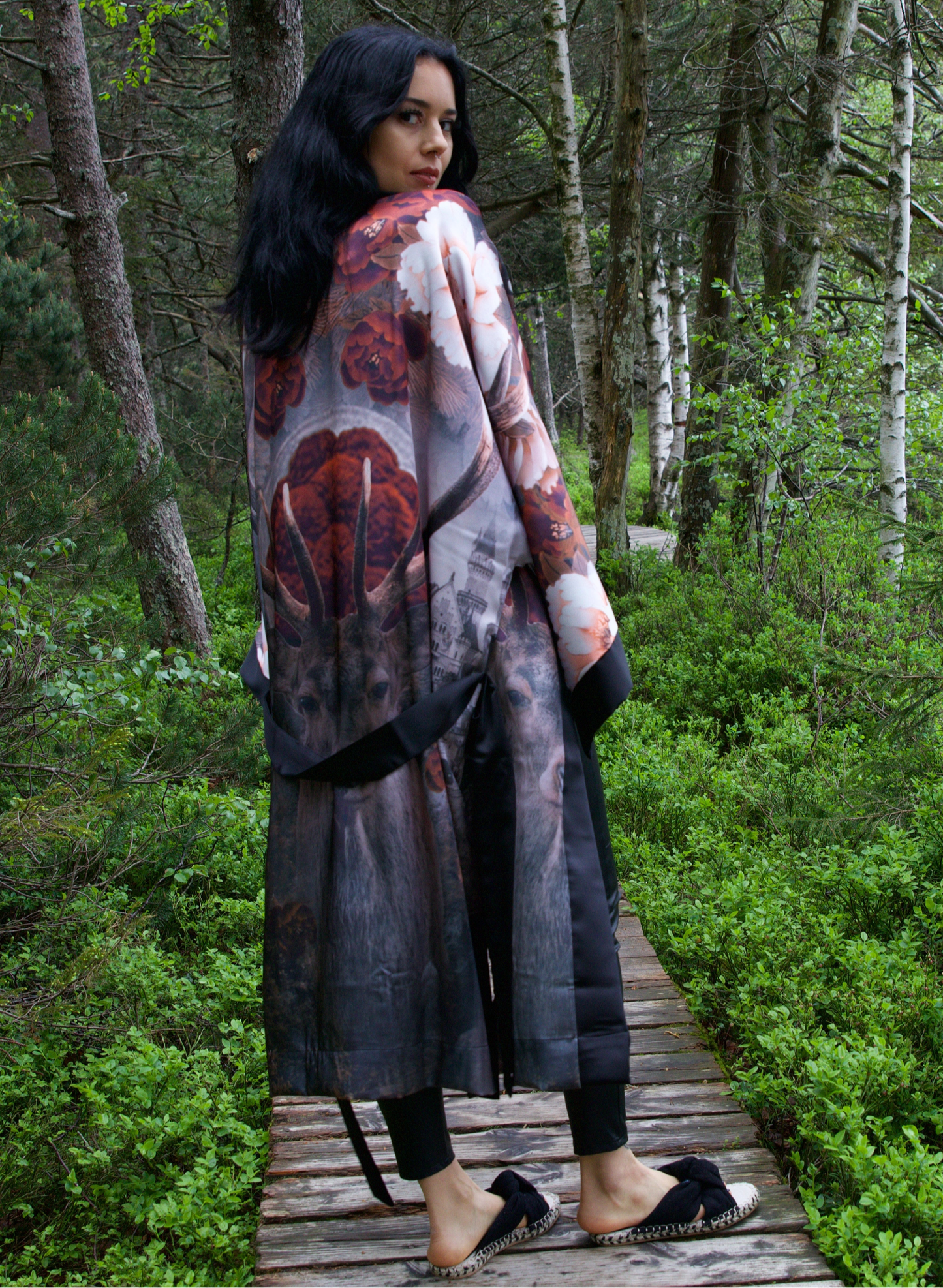 Woman in a patterned coat standing on a wooden path in a forest