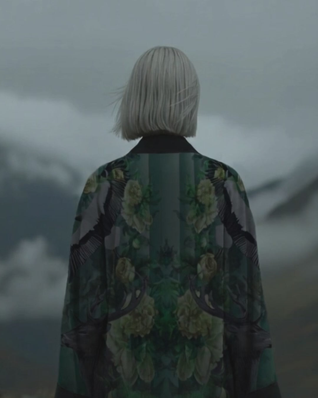 Designer long kimono with rich jade green nature print, modeled in a dramatic cloudy mountain setting